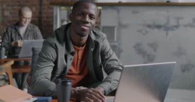 İş yerinde laptopla masada oturan kendine güvenen Afro-Amerikan bir adamın yavaş çekim portresi. İş ve insan kavramı.