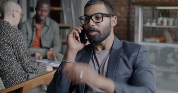 現代のコワーキングオフィスに座っている携帯電話のビジネスを議論するアラブ起業家 スーツのビジネスマンはプロの会話に集中しました — ストック動画