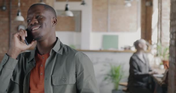 兴高采烈的非裔美国男人站在合作中心 一边用手机聊天 一边喝着咖啡 交流和戒酒的概念 — 图库视频影像
