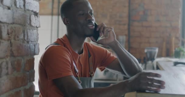 在现代咖啡馆里 快乐的非洲裔美国男人在围裙上和客户用手机交谈 通信和咖啡屋概念 — 图库视频影像