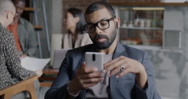 スマートフォンのスワイプ画面を使用したビジネスマンのスローモーションと カフェのワイヤレスイヤホンで音楽を聴く 人とガジェットのコンセプト — ストック動画