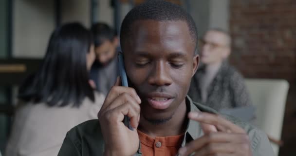 明るいアフリカ系アメリカ人男性の従業員は ぼやけたオフィスの背景に対して携帯電話で話しています コミュニケーションと職場コンセプト — ストック動画