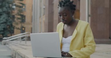 Zeki, Afro-Amerikan kadın, dışarıda, şehir sokağında dizüstü bilgisayarla çalışıyor. Serbest meslek ve teknoloji kavramı.