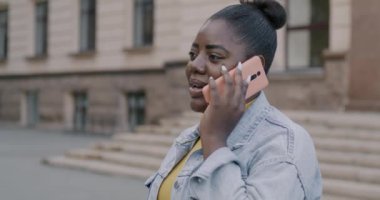 Neşeli Afro-Amerikan bayan cep telefonuyla konuşuyor. Cihazla konuşuyor. Açık havada sohbetin tadını çıkarıyor. Teknoloji ve iletişim konsepti.