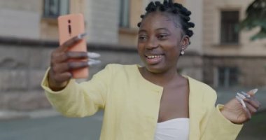 Kaygısız Afrikalı Amerikalı kadın konuşuyor ve şehirdeki akıllı telefonuyla çevrimiçi video görüşmesinin tadını çıkarıyor. İletişim ve gençlik kavramı.
