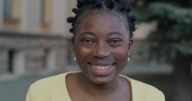 Şehirli bulanık arka planda kameraya bakarken gülümseyen Afro-Amerikan kadının yavaş çekim portresi. İnsanlar ve duygu kavramı.