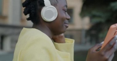 Neşeli Afrikalı Amerikalı kadınların dışarıda dans edip kulaklıkla müzik dinlemeleri. Milenyum ve eğlence konsepti.