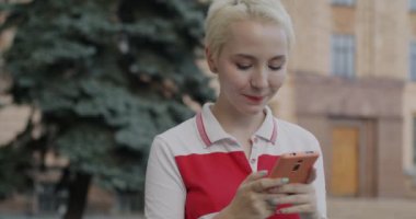 Kaygısız genç kız öğrenci akıllı telefonuyla sosyal medyayı kontrol ediyor ve dışarıda gülüyor. Gadget ve milenyum konsepti.