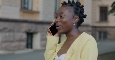 Kaygısız Afrikalı Amerikalı kadın cep telefonuyla konuşuyor. Şehir caddesinde konuşmaktan keyif alıyor. İletişim ve insan kavramı.