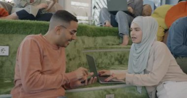 Müslüman kadın, Arap erkekle konuşuyor ve yaratıcı ortak çalışma merkezinde dizüstü bilgisayarla çalışıyor. İş iletişimi ve işbirliği kavramı.