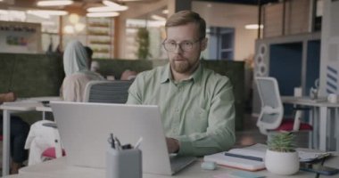 Hırslı iş adamı dizüstü bilgisayar kullanıyor ve gözlük tamir ediyor. Ortak ofiste çalışmaya odaklanmış. İş yeri ve mesleki meslek kavramı.