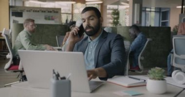 Kendine güvenen Orta Doğulu iş adamı cep telefonuyla konuşuyor ve birlikte çalışma merkezinde dizüstü bilgisayara danışmanlık yapıyor. İnsanlar ve iletişim konsepti.
