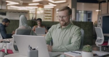 İş adamı internetten bilgisayar ve kablosuz kulaklıkla konuşma yapıyor ve açık uzay ofisinde el sallıyor. İletişim ve teknoloji kavramı.