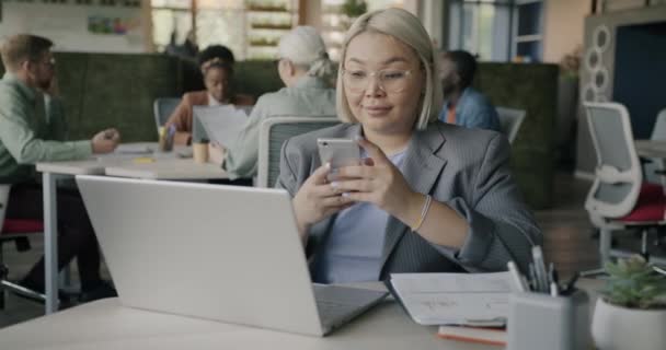 快乐的年轻女性在开放的办公室里用智能手机发短信与客户沟通 现代技术和商业通信概念 — 图库视频影像