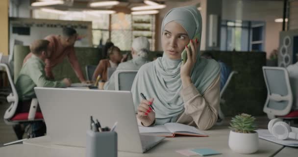 Vänlig Muslimsk Kvinna Talar Mobiltelefon Till Klient Och Använder Laptop — Stockvideo