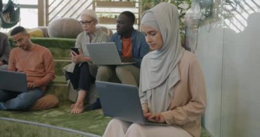 Dizüstü bilgisayarla çalışan Müslüman bir kadın çalışma alanında Afrikalı Amerikalı meslektaşıyla konuşuyor. İş adamları ve işbirliği kavramı.