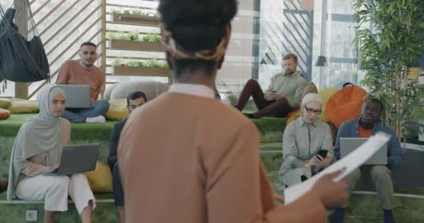 マネージャーのアフリカ系アメリカ人女性は 現代のコワーキングスペースでクリップボードを指す多様なチームと話しています チームワークとキャリアコンセプト — ストック動画
