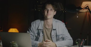 Karanlık bir iş yerinde masa başında oturan ve geceleri kameraya bakan erkek ofis çalışanının portresi. İş kavramında insanlar ve son teslim tarihi.