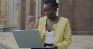 Neşeli Afro-Amerikalı iş kadını internette bilgisayarla konuşuyor ve şehirde el sallıyor. İletişim ve internet bağlantısı kavramı.