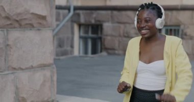 Şehirde yürüyen ve kulaklıkla müzik dinleyen mutlu Afrikalı Amerikalı kadın. Eğlence ve şehir yaşam tarzı konsepti.
