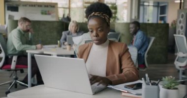 Ciddi bir Afro-Amerikalı kadın bilgisayarı paylaşılan ofisteki uzak aktivitelere odaklıyor. İletişim ve modern teknoloji kavramı.