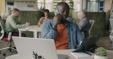 İş danışmanı Afrikalı Amerikalı adam cep telefonuyla konuşuyor ve ortak ofisteki belgeleri kontrol ediyor. Ortak çalışma ve kurumsal iletişim konsepti.