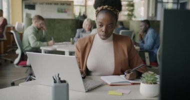 Hırslı Afrikalı Amerikalı iş kadını laptopla çalışıyor ve çalışma merkezinde masa başında araştırma yazıyor. Modern teknoloji ve insan kavramı.