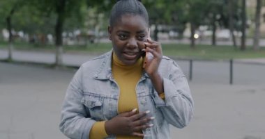 Aşırı neşeli Afro-Amerikan kadın cep telefonuyla konuşuyor gülümsüyor ve dışarıda neşe saçıyor. İletişim ve insan kavramı.