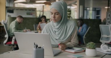 Başörtüsü içinde güzel bir Müslüman kadın bilgisayar ve kredi kartıyla online ödeme yapıyor. Çalışma merkezinde masada oturuyor. Finans ve bankacılık kavramı.