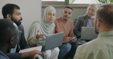 Başarılı genç iş arkadaşları çember oluşturup iş konuşuyorlar ve ortak çalışma alanında dizüstü bilgisayar kullanıyorlar. Modern yaşam tarzı ve başlangıç konsepti.