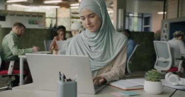Müslüman iş kadını dizüstü bilgisayarla yazı yazıp aynı ofiste çalışarak tesettüre giriyor. İstihdam ve İslam kavramı.
