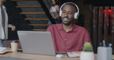 Neşeli ofis çalışanı kulaklıkla müzik dinliyor dans ediyor ve dizüstü bilgisayarla çatı katında çalışıyor. İnsanlar ve işyeri eğlence konsepti.