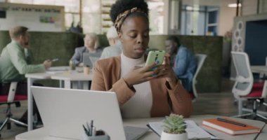 Neşeli Afro-Amerikan bayan akıllı telefon mesajları kullanıyor açık uzay ofisinde modern iletişimin tadını çıkarıyor. Teknoloji ve insanlar kavramı.