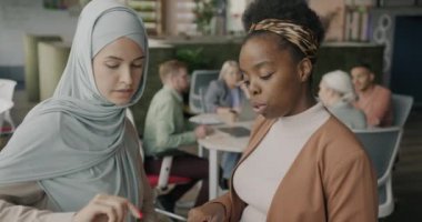 Genç kadınlar iş belgelerini tartışıyor sonra da açık uzay ofisinde iş arkadaşlarıyla konuşuyorlar. İletişim ve kurumsal faaliyet kavramı.