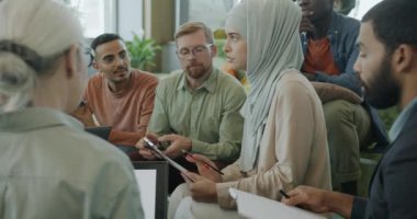 Başarılı Müslüman kadın, modern çalışma ofisinde çeşitli kişilerle iş arkadaşlarıyla konuşuyor. İş adamları işbirliği ve girişimi tartışıyor.
