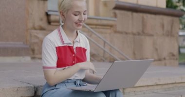 Duygusal genç bir kadın internette bilgisayar sohbeti yapıyor ve şehirdeki merdivenlerde el sallıyor. İletişim ve milenyum yaşam tarzı konsepti.