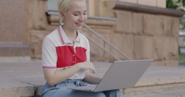 Duygusal genç bir kadın internette bilgisayar sohbeti yapıyor ve şehirdeki merdivenlerde el sallıyor. İletişim ve milenyum yaşam tarzı konsepti.