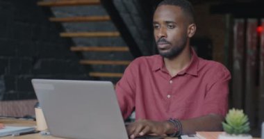Dizüstü bilgisayarla çalışan kendine güvenen Afro-Amerikan iş adamı. Sonra kameraya dönüp çatı katında gülümsüyor. İş ve mesleki meslek kavramı.