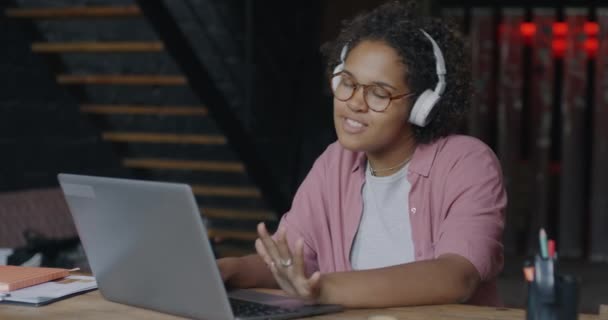 ハッピーアフリカ系アメリカ人のビジネスレディーは ラップトップコンピュータで作業し コワーキングオフィスでヘッドフォンで音楽を聴いています 仕事とエンターテイメントのコンセプト — ストック動画