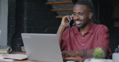 Cep telefonuyla konuşan, iş konuşan ve çatı katında dizüstü bilgisayar kullanan Afrikalı Amerikalı bir çalışan. İş ve iletişim konsepti.
