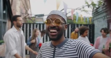 Aşırı neşeli Afrikalı Amerikalı adam açık hava partisinde dans eden arkadaşlarının kadeh kaldırdığını gösteren bir konuşma yapıyor. İletişim ve modern yaşam tarzı kavramı.