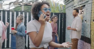 Neşeli Afrikalı Amerikalı kadın cep telefonuyla konuşuyor açık hava partisi sırasında sokak kafesinde gülüyor. Gençlik ve cep telefonu bağlantısı kavramı.
