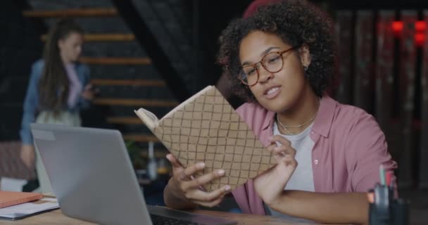 聪明的非洲裔美国女商人坐在富有创造力的工作岗位上看书 微笑着坐在办公桌前 文学与成功人士概念 — 图库视频影像