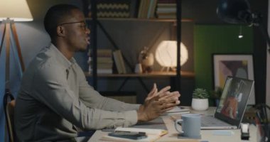 Afrika kökenli Amerikalı erkek meslektaşlar gece ofiste görüntülü görüşme yaparken konuşuyorlar. İş iletişimi ve modern teknoloji kavramı.