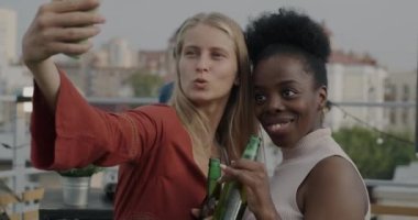 Genç Afro-Amerikan ve Kafkasyalı kadınlar akıllı telefon kameralarına poz veriyorlar ve partilerde kentin arka planında selfie çekiyorlar. Arkadaşlık ve modern yaşam tarzı kavramı.