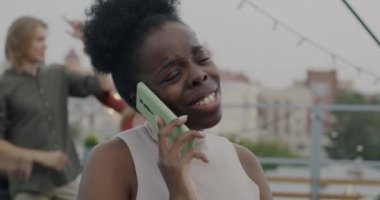 Genç Afrikalı Amerikalı kadın cep telefonuyla konuşuyor çatıdaki partide yüksek sesli müzik eşliğinde bağırıyor. Modern teknoloji ve iletişim konsepti.