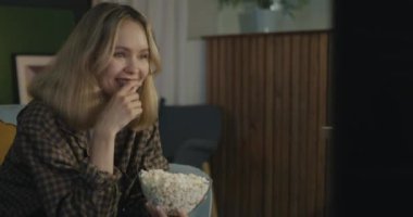 Komik komedi seyreden ve gülen, TV yiyen mutlu genç bir bayan dairede tasasız bir akşamın tadını çıkarıyor. Milenyum ve kitle iletişim araçları kavramı.