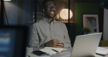Afrika kökenli Amerikalı çalışan internette konuşma yapıyor. Gece karanlık ofiste dizüstü bilgisayar kullanarak iyi bir hareket yaptığını gösteriyor. İletişim ve başarılı iş kavramı.