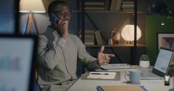 アフリカ系アメリカ人のオフィスワーカーが携帯電話で話し 夕方には暗いオフィスで働くメモを取った ビジネスコミュニケーションと仕事のコンセプト — ストック動画