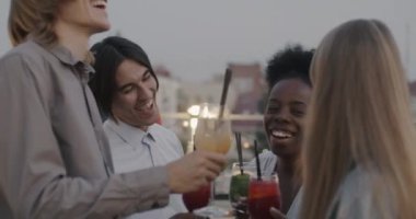 Şık giyinmiş bir grup arkadaş bardaklarını tokuşturup çatıdaki partide bayramı kutluyorlar. Kutlama ve modern eğlence konsepti.